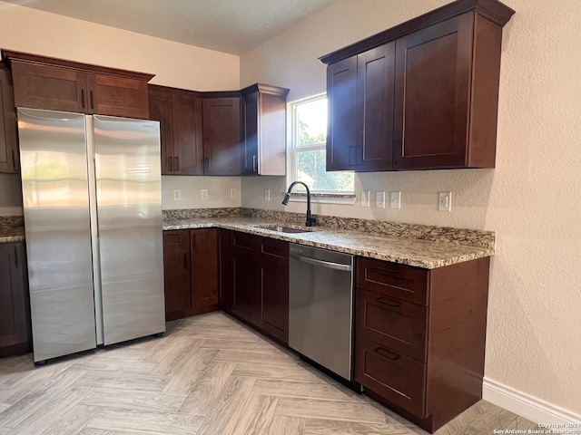 kitchen with appliances with stainless steel finishes, light stone counters, sink, and dark brown cabinetry