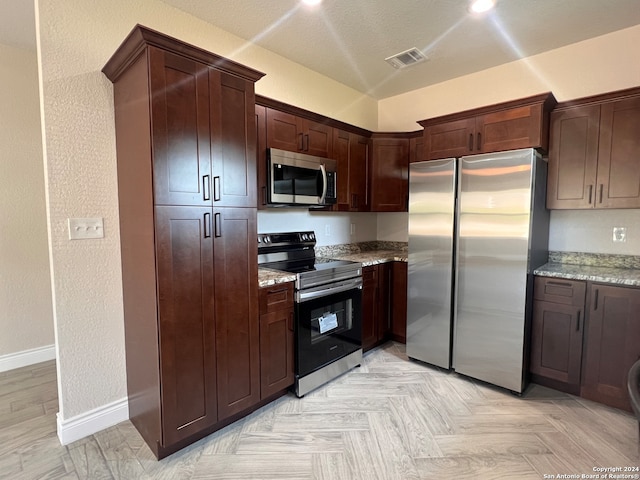 kitchen featuring a textured ceiling, light stone countertops, appliances with stainless steel finishes, and lofted ceiling