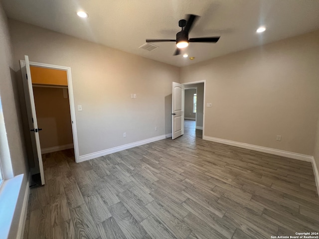 unfurnished bedroom with a walk in closet, wood-type flooring, a closet, and ceiling fan