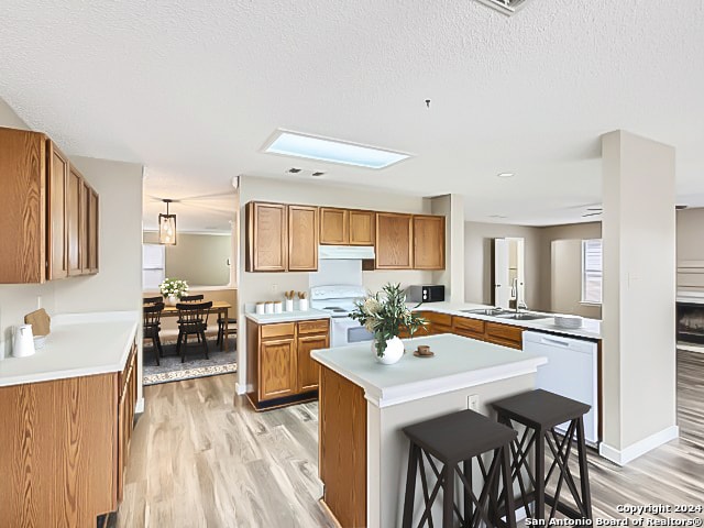 kitchen with a breakfast bar area, white appliances, hanging light fixtures, kitchen peninsula, and a skylight