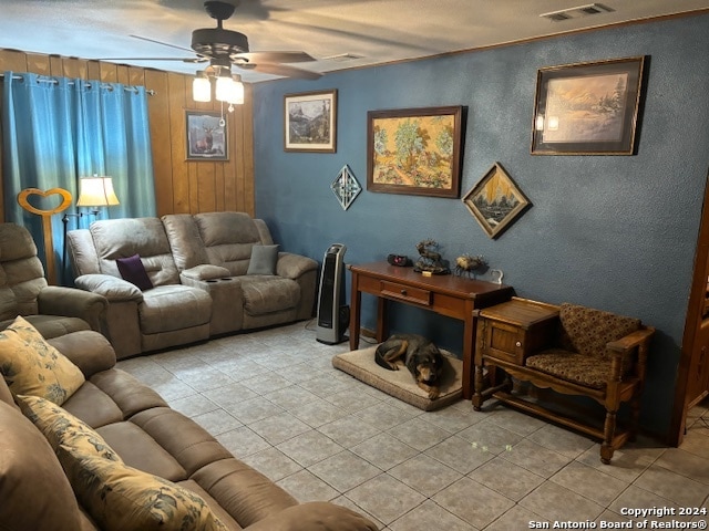 living room featuring ceiling fan, light tile patterned floors, and wooden walls