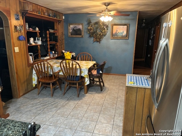 tiled dining area featuring ceiling fan and wooden walls