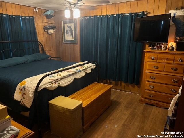 bedroom with ceiling fan, wooden walls, and dark hardwood / wood-style flooring