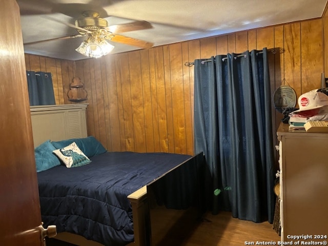 bedroom with ceiling fan, wood walls, and light wood-type flooring