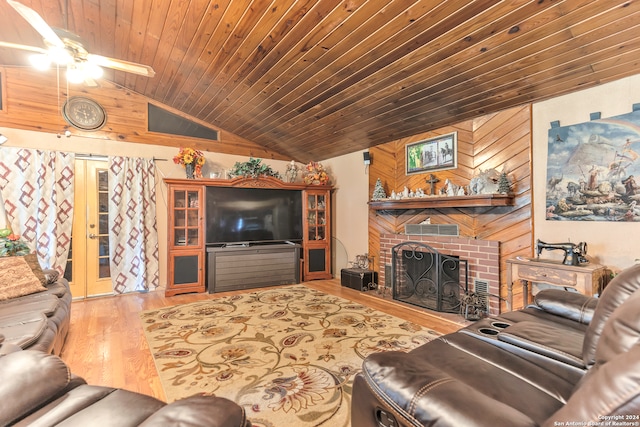 living room with light wood-type flooring, wood walls, a brick fireplace, ceiling fan, and vaulted ceiling