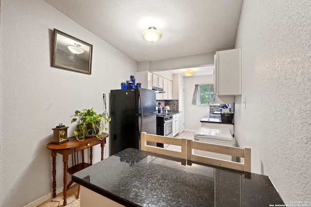 kitchen with white cabinets, black refrigerator, stainless steel range, decorative backsplash, and kitchen peninsula