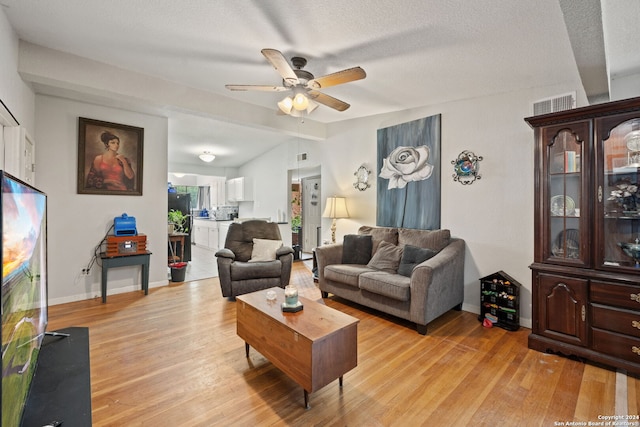 living room with ceiling fan, a textured ceiling, and light hardwood / wood-style flooring