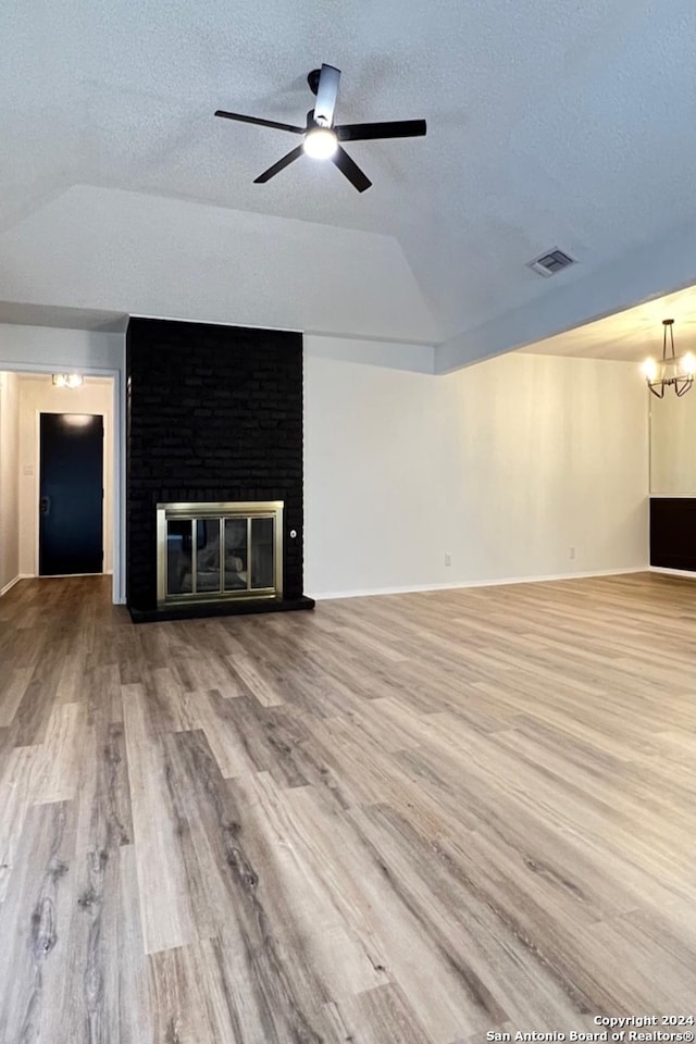 unfurnished living room with lofted ceiling, ceiling fan with notable chandelier, a fireplace, and light hardwood / wood-style flooring