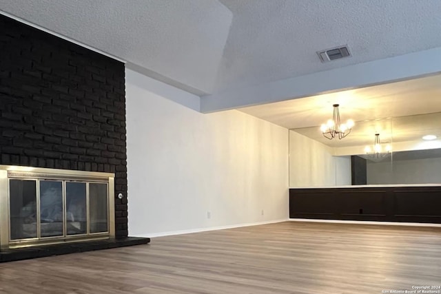 empty room with a textured ceiling, hardwood / wood-style floors, a brick fireplace, and a chandelier