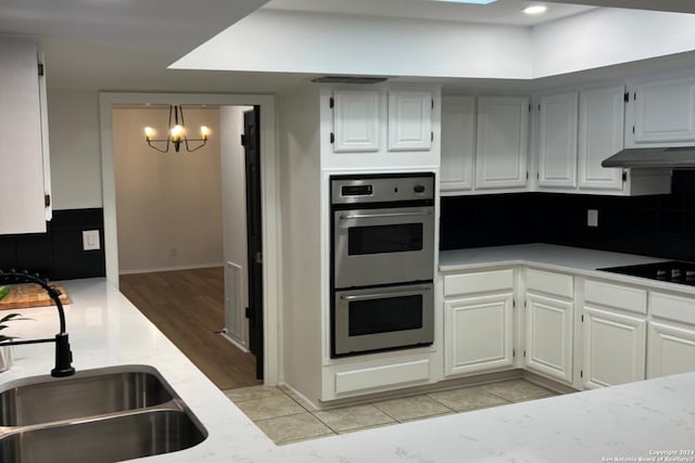 kitchen featuring an inviting chandelier, light hardwood / wood-style floors, stainless steel double oven, sink, and black electric stovetop