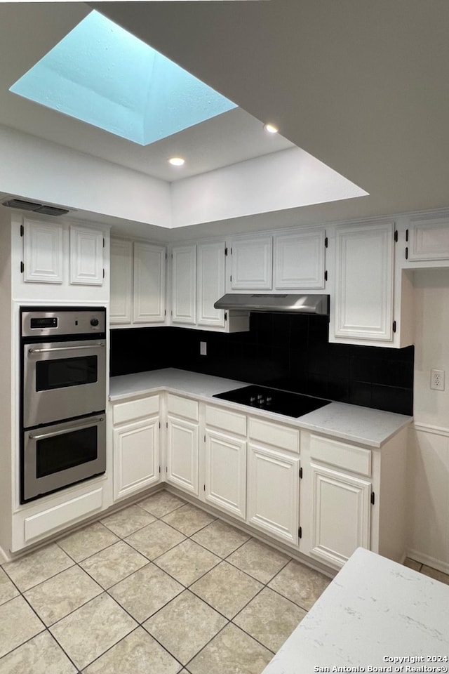 kitchen featuring light tile patterned floors, stainless steel double oven, white cabinetry, a skylight, and black electric cooktop