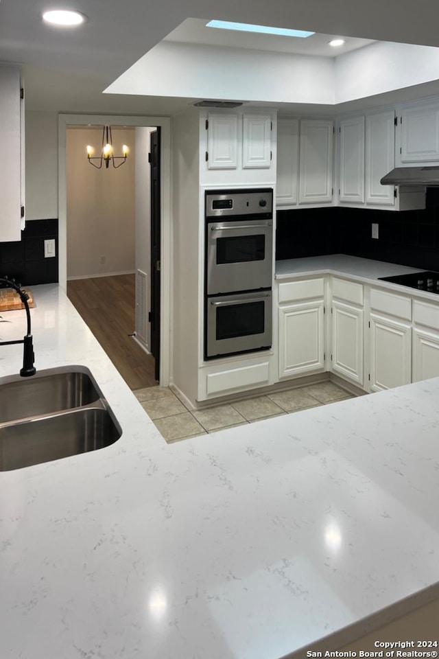 kitchen featuring a notable chandelier, backsplash, sink, black electric cooktop, and light wood-type flooring