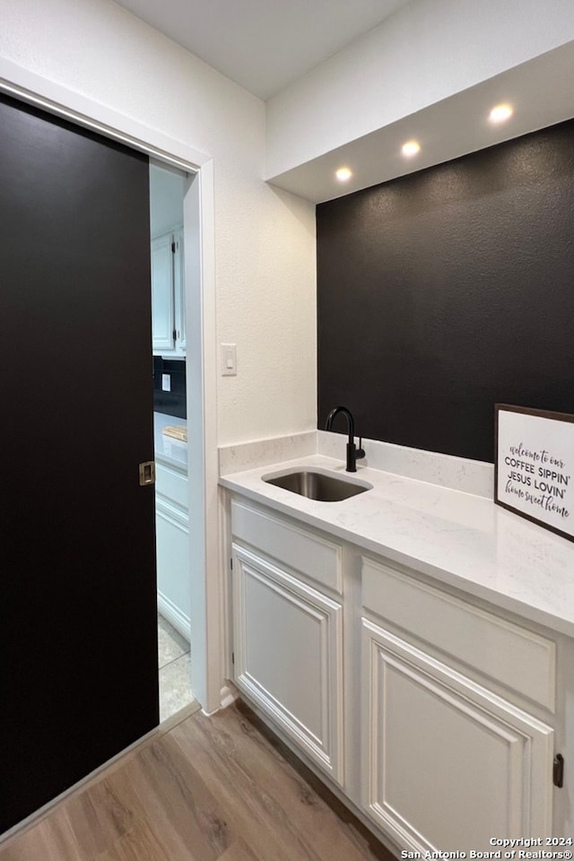 interior space with light wood-type flooring, white cabinetry, light stone counters, and sink