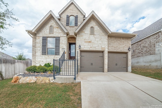 french provincial home featuring brick siding, an attached garage, a front lawn, fence, and driveway