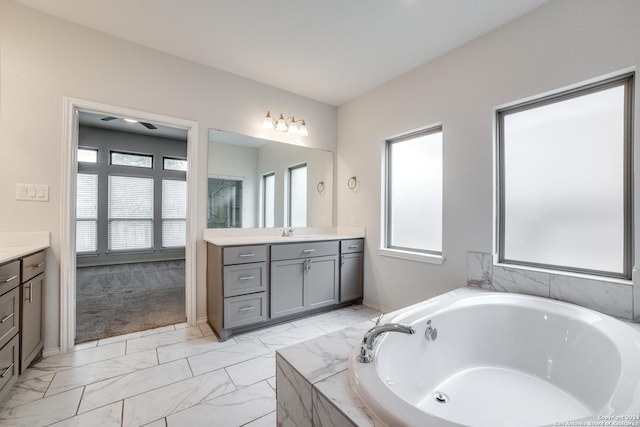 full bathroom with vanity, a bath, baseboards, and marble finish floor