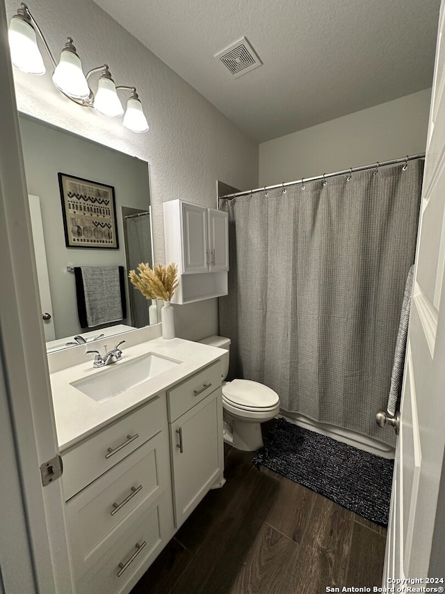 bathroom featuring wood-type flooring, a textured ceiling, a shower with shower curtain, toilet, and vanity