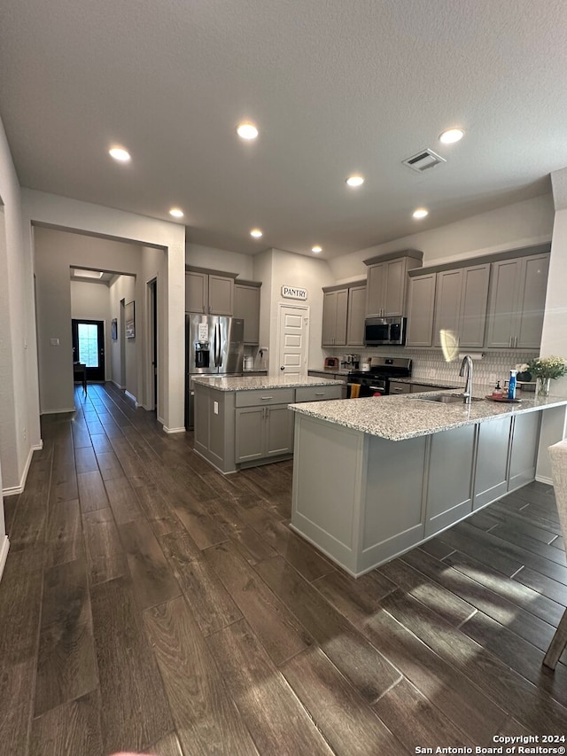 kitchen featuring light stone counters, backsplash, dark wood-type flooring, gray cabinets, and stainless steel appliances