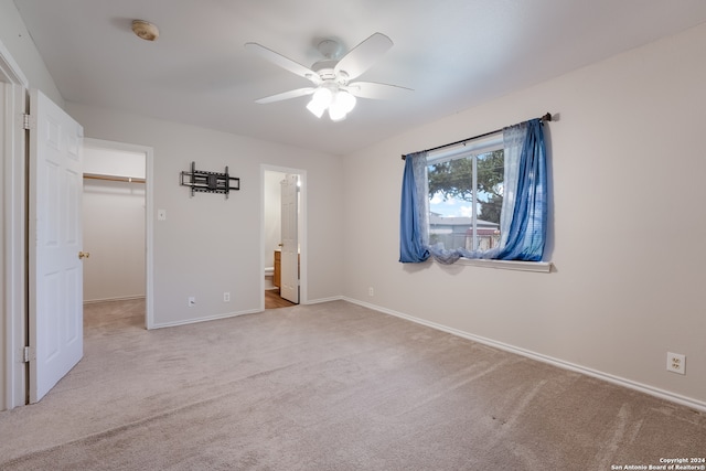 unfurnished bedroom with ensuite bathroom, light carpet, a walk in closet, a closet, and ceiling fan