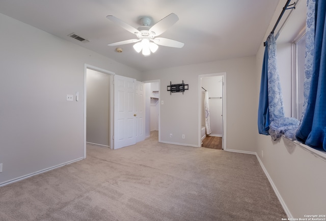 unfurnished bedroom with a walk in closet, ceiling fan, light carpet, and ensuite bath