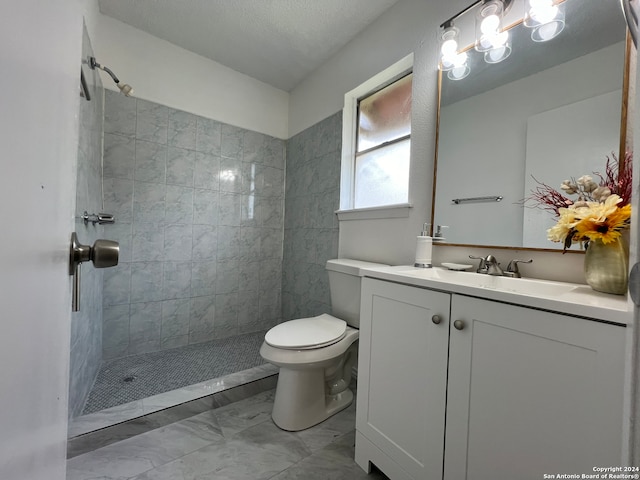 bathroom with toilet, vanity, a textured ceiling, and a tile shower