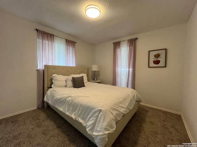 bedroom with multiple windows, dark colored carpet, and a textured ceiling