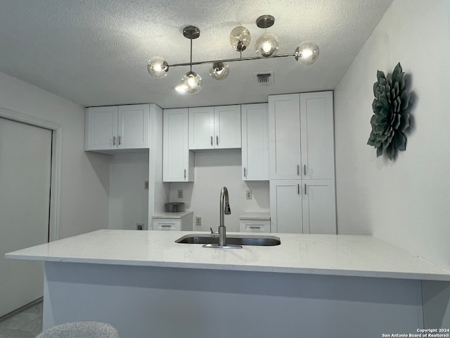 kitchen featuring white cabinetry, hanging light fixtures, sink, and light stone countertops