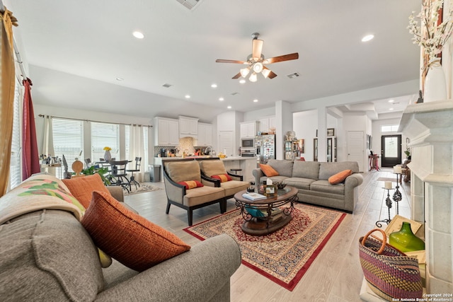 living room featuring a healthy amount of sunlight, ceiling fan, a high end fireplace, and light wood-type flooring