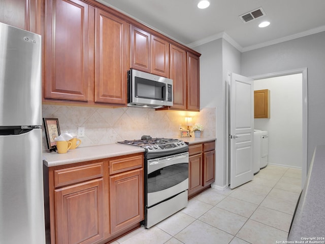 kitchen featuring appliances with stainless steel finishes, light tile patterned flooring, decorative backsplash, ornamental molding, and washing machine and dryer