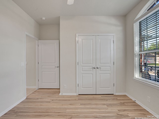 unfurnished bedroom featuring multiple windows, light hardwood / wood-style flooring, ceiling fan, and a closet