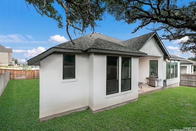 rear view of property with a yard, roof with shingles, a fenced backyard, and stucco siding