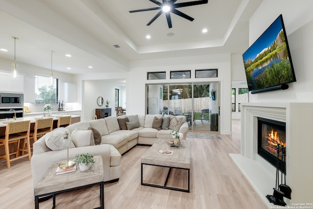 living room with light wood-type flooring, a tray ceiling, and ceiling fan