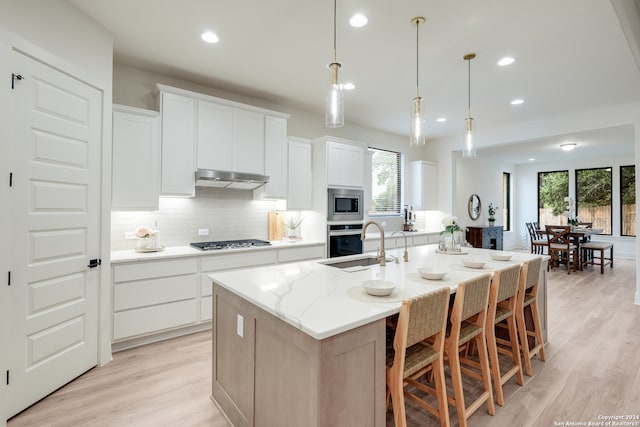 kitchen with a healthy amount of sunlight, stainless steel appliances, white cabinets, and a center island with sink