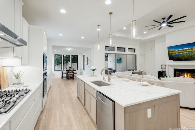 kitchen featuring light stone countertops, a center island with sink, stainless steel appliances, sink, and white cabinetry