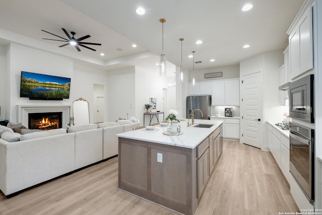 kitchen with a sink, open floor plan, light wood-type flooring, a lit fireplace, and appliances with stainless steel finishes