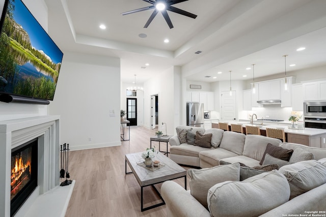 living area with recessed lighting, light wood-type flooring, a ceiling fan, and a tray ceiling