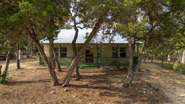 view of front of house with a standing seam roof, stone siding, fence, covered porch, and metal roof