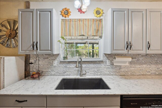 kitchen featuring light stone countertops, black dishwasher, tasteful backsplash, and sink