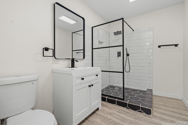 bathroom with hardwood / wood-style floors, toilet, a tile shower, and vanity