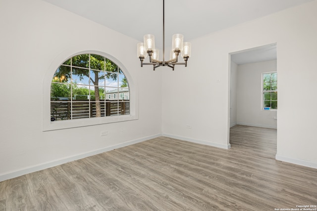 unfurnished room with a notable chandelier and light wood-type flooring