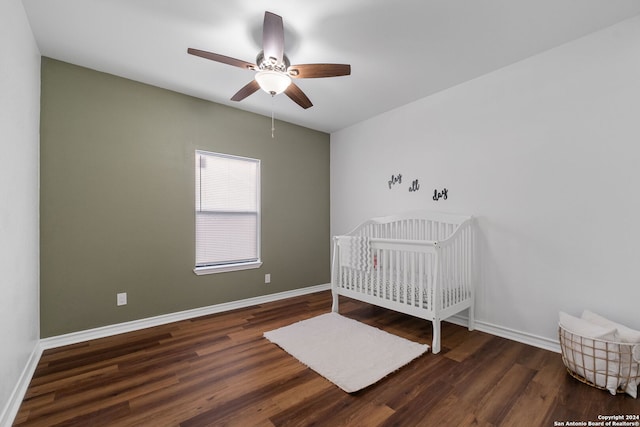 unfurnished bedroom with dark wood-type flooring, ceiling fan, and a crib