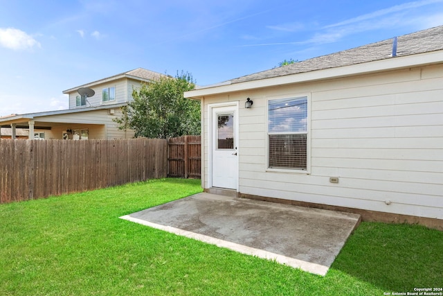 view of exterior entry with fence, a lawn, a shingled roof, and a patio area