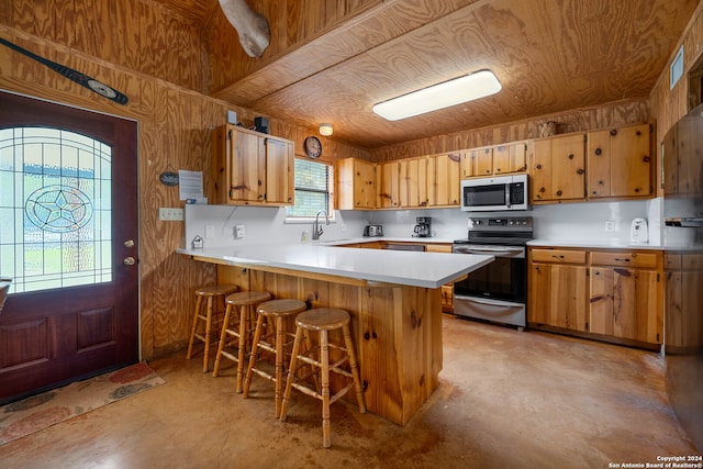 kitchen featuring wood walls, a kitchen breakfast bar, sink, kitchen peninsula, and stainless steel appliances