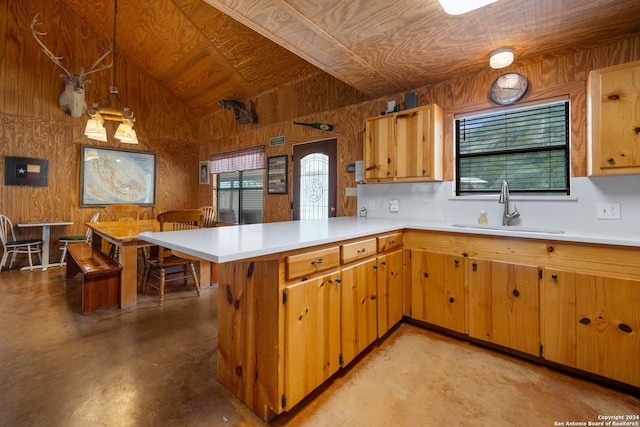 kitchen featuring sink, kitchen peninsula, pendant lighting, vaulted ceiling, and wooden walls