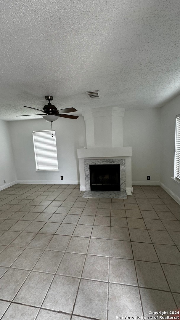 unfurnished living room with ceiling fan, light tile patterned floors, a high end fireplace, and a textured ceiling