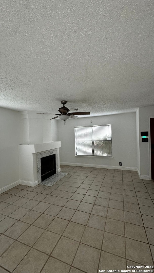 unfurnished living room with a textured ceiling, ceiling fan, a high end fireplace, and light tile patterned floors