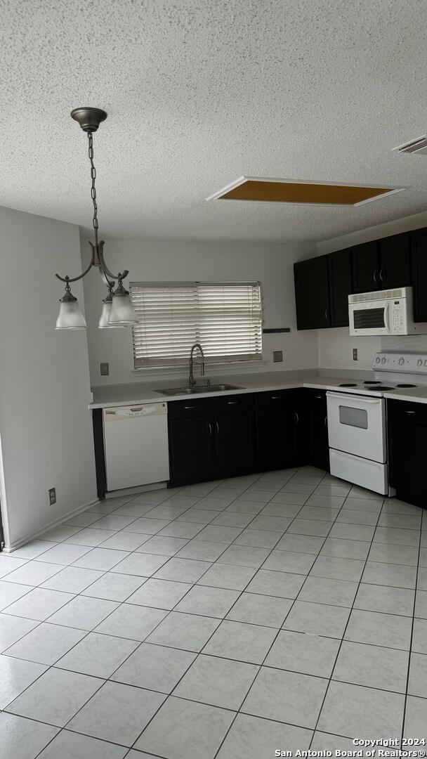 kitchen featuring a textured ceiling, decorative light fixtures, white appliances, sink, and light tile patterned flooring