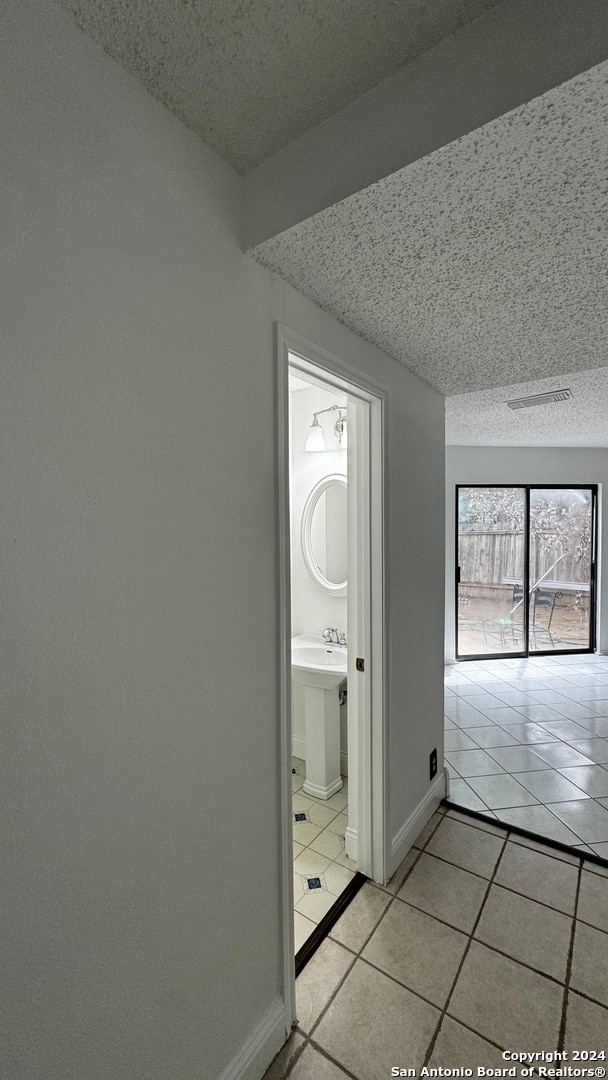 hallway with a textured ceiling and light tile patterned floors