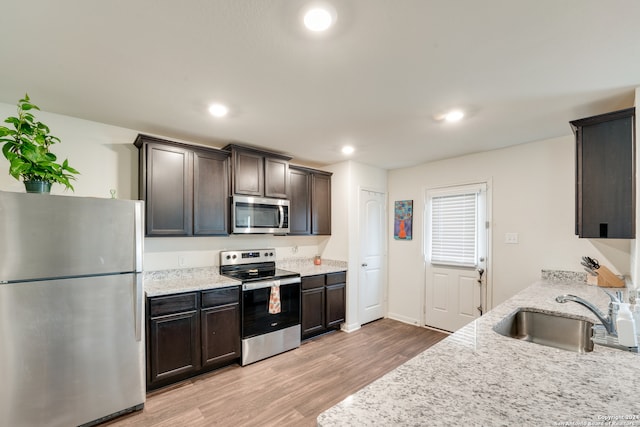 kitchen featuring dark brown cabinets, light hardwood / wood-style flooring, appliances with stainless steel finishes, sink, and light stone counters