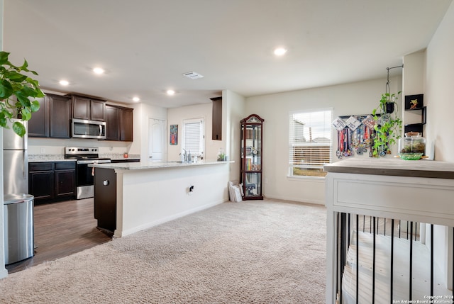 kitchen featuring dark hardwood / wood-style flooring, light stone counters, stainless steel appliances, and dark brown cabinetry