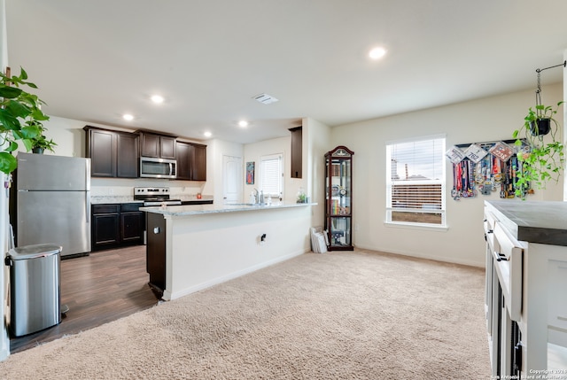 kitchen featuring appliances with stainless steel finishes, light stone counters, hardwood / wood-style floors, and dark brown cabinetry